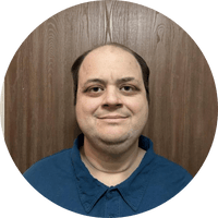 photo of a man's face. He's standing in front of a panelled wall and wearing a navy blue polo shirt